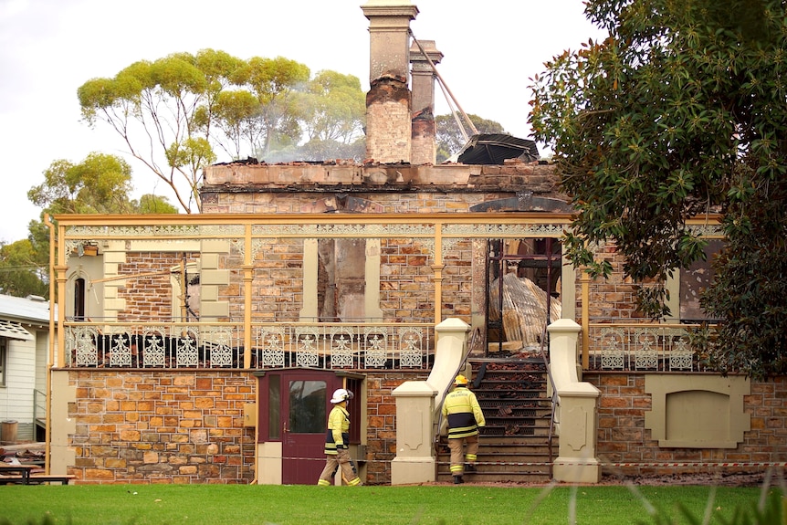 Two firefighters walk towards the stair entrance of an historic looking building damaged by fire.