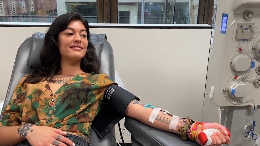 A tattooed woman sitting in a chair donating plasma.