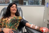 A tattooed woman sitting in a chair donating plasma.