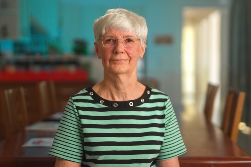Woman with white hair and glasses wearing a striped green and black shirt. 