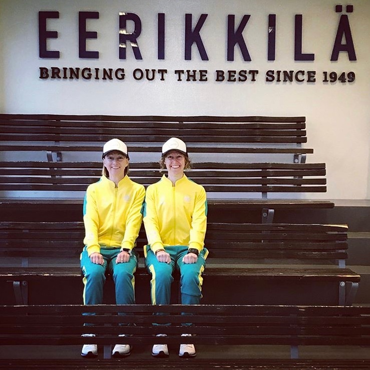 Two women smile on a bench in Australia tracksuits