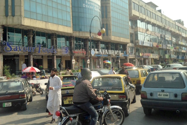 Vehicle traffic and pedestrians travel through a main street in Islamabad's business district.