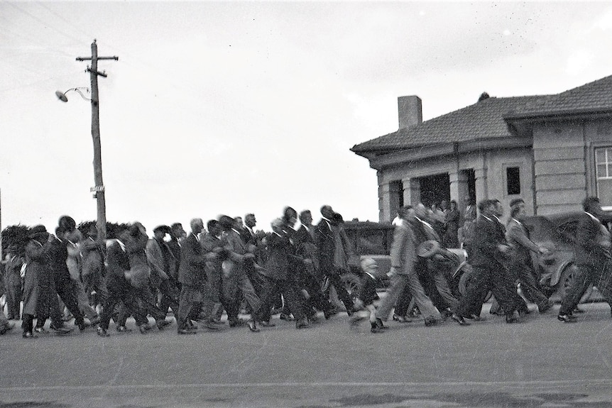 A historic photo showing a large group of men in suits march through a town.