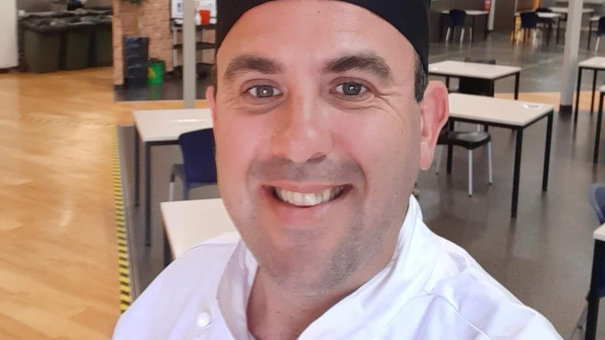 Selfie of man in chef's hat and white uniform with kitchen in background