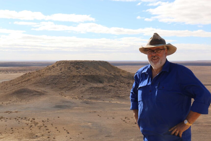 Medium portrait shot of a man in a blue shirt standing on the edge of an outback plateau.