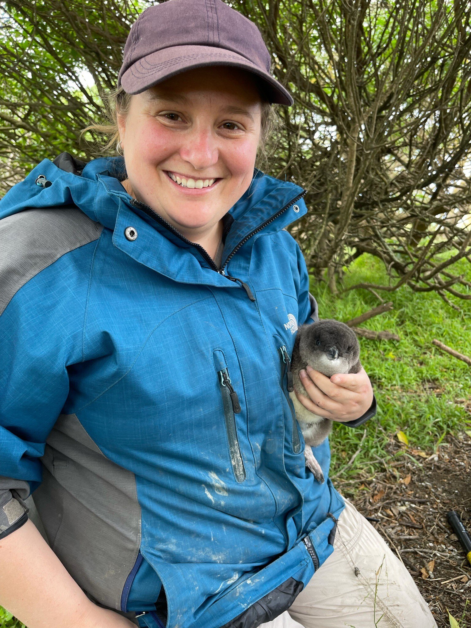 A woman outdoors, smiling while she holds a little penguin in her hand.