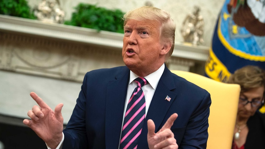 President Donald Trump holds his hands up as he speaks while sitting on a chair.