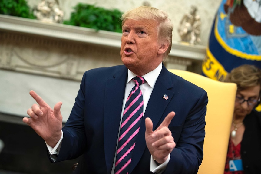 President Donald Trump holds his hands up as he speaks while sitting on a chair.