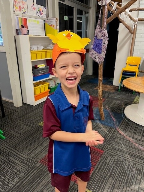 A young boy in a school uniform laughs at the camera.