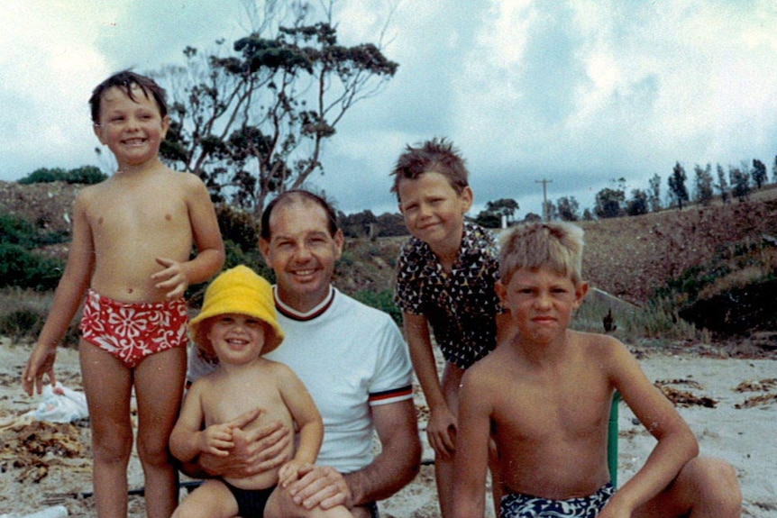 A group of boys around a father at a beach in the 70s.