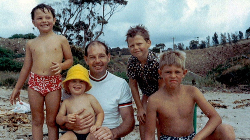 A group of boys around a father at a beach in the 70s.