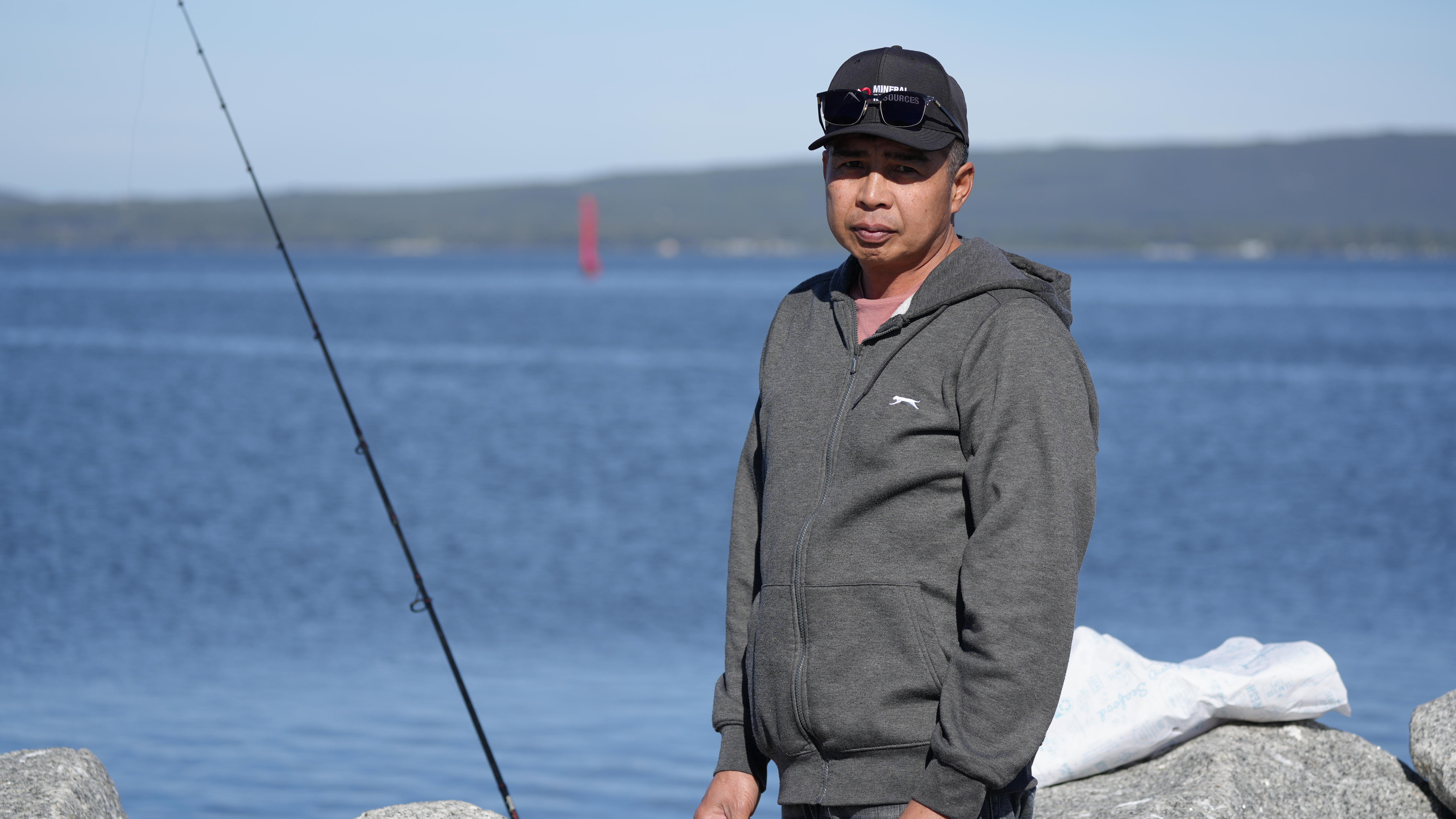 A man wearing a black cap with ocean in background and fishing rod on left.