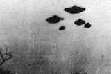 A grainy black and white photo shows three UFOs in the sky