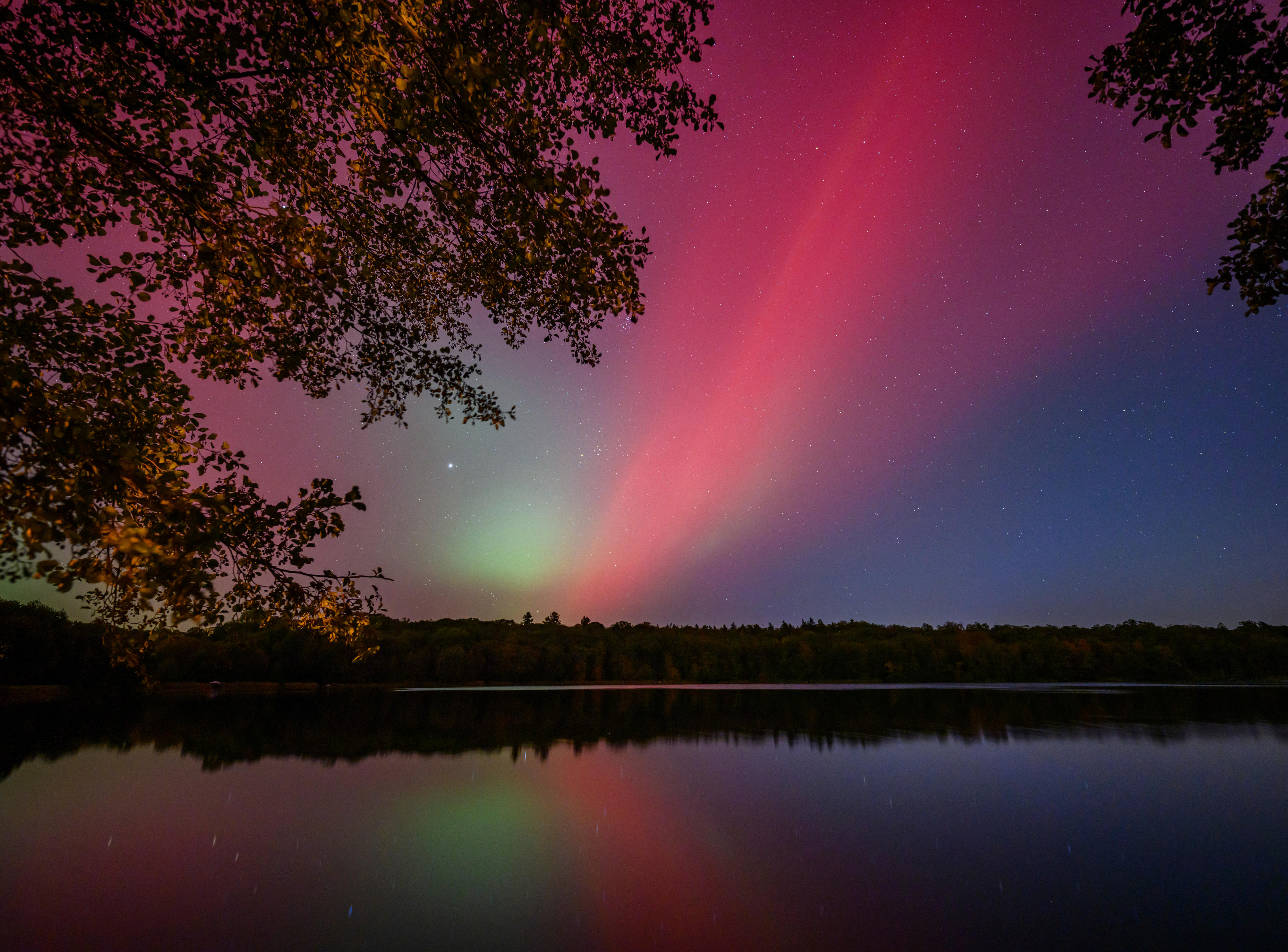 Pink northern lights shine in the night sky over the Black Lake