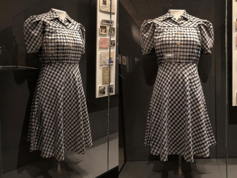 A dress made out of blue and white checked fabric hangs in a display cabinet at the Australian War Memorial.