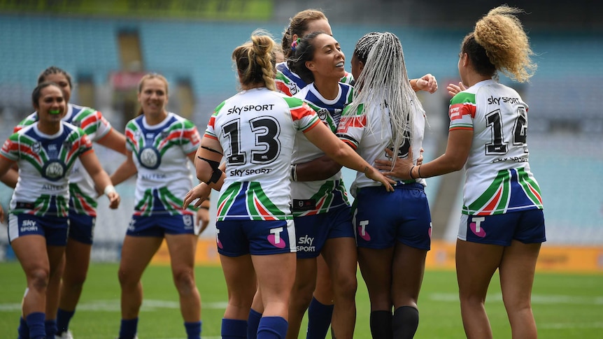 A group of NRLW players gather around a tryscorer in celebration as the ball drops to the turf.
