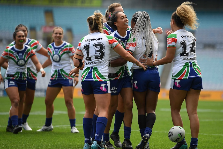 A group of NRLW players gather around a tryscorer in celebration as the ball drops to the turf.