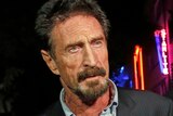 John McAfee in a suit looking right of screen with neon signs in the background