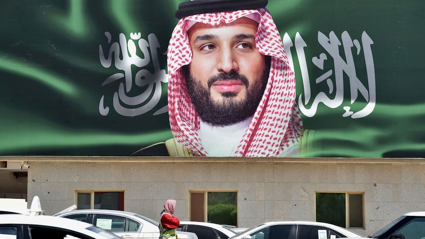 A large poster of an Arabic man with a white and red head cover on a green background, with traffic and a single person in front