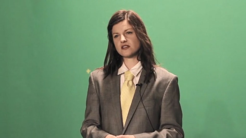 Woman with a jacket and tie on stands in front of a green screen