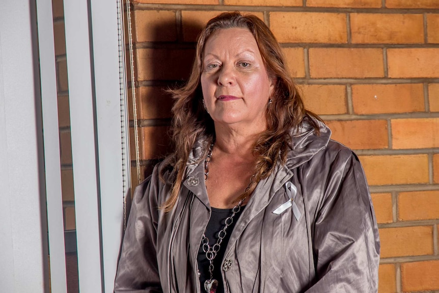 A woman against a brick wall wearing a white ribbon on her jacket