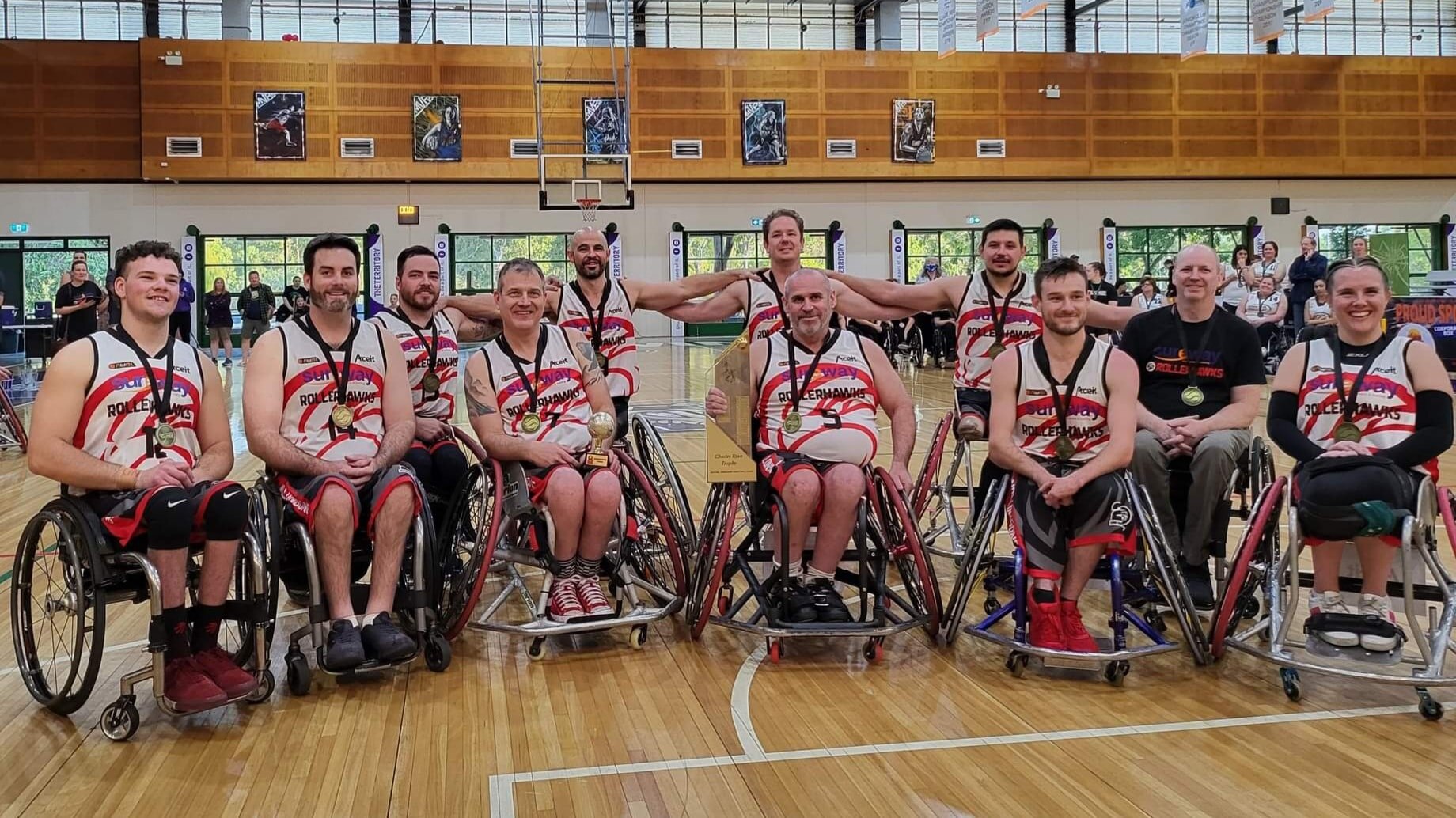 A wheelchair basketball team arrayed on a court, all smiling and wearing medals.