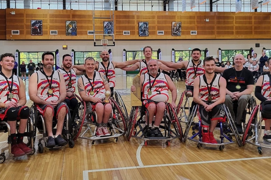 A wheelchair basketball team arrayed on a court, all smiling and wearing medals.