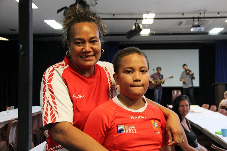 A woman from Tonga stands in a community hall with her son.