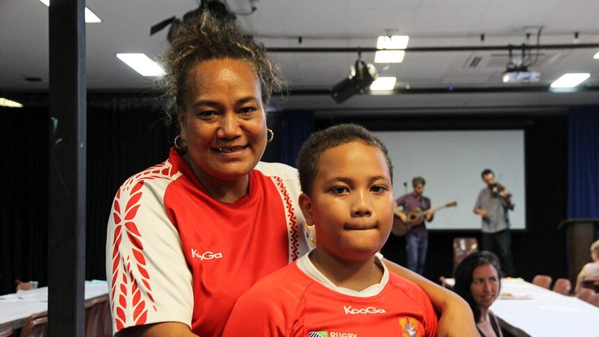 A woman from Tonga stands in a community hall with her son.