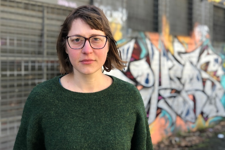 A woman stands with street art on a wall behind her.