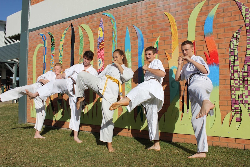 Five karate students practice their technique outside against a wall.