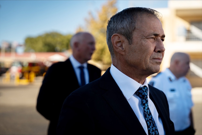 WA Premier Roger Cook stands looking to the right of frame wearing a suit and looking very serious.