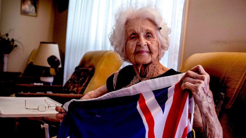 An elderly woman looks at the camera holding an Australian flag