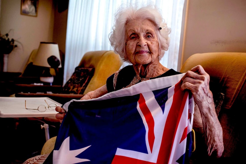 An elderly woman looks at the camera holding an Australian Flag.