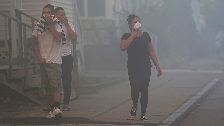 Three residents walk down a smoke-filled street covering their nose and mouths