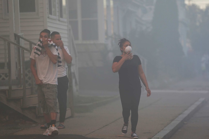 Three residents walk down a smoke-filled street covering their nose and mouths