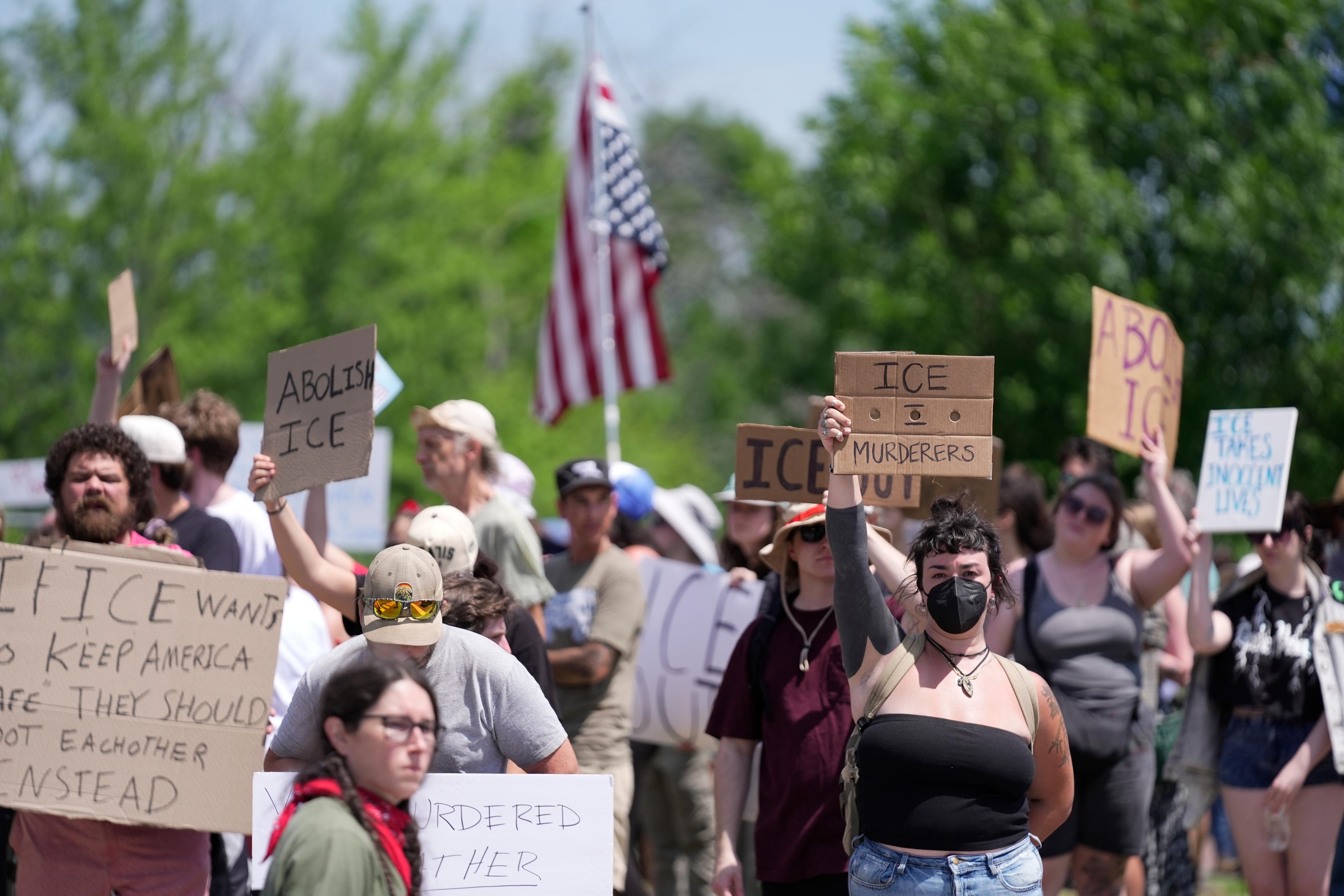 Protesters stand in a group holding cardboards signs with anti-ICE slogans.