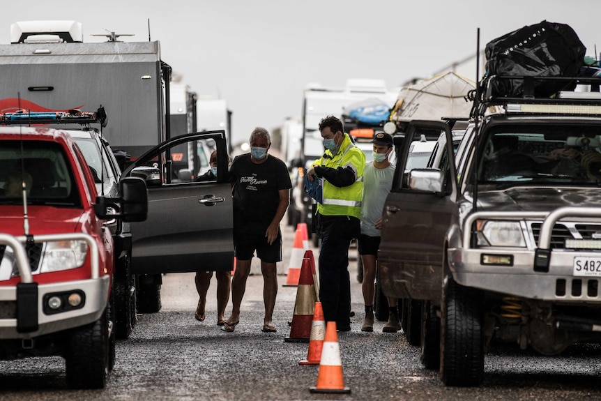 Motorists and a man in a hi vis vest stand inbetween vehicles at the Eucla border checkpoint.