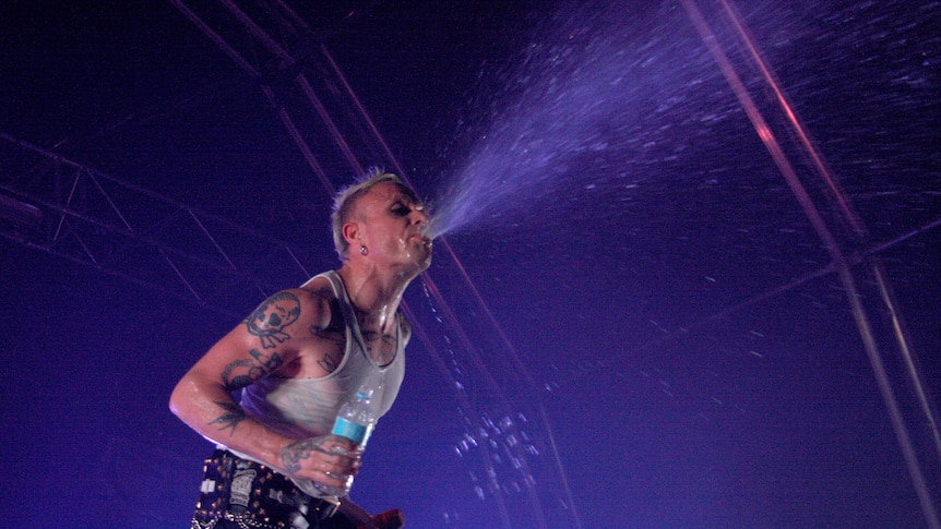 Keith Flint, wearing a white singlet, spits water into the crowd from the stage.