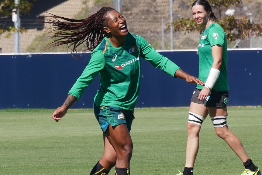 Young lady in green long sleeve shirt laughing while walking on a rugby field.