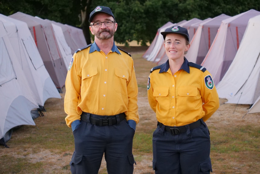 A man and woman in yellow uniform stand in front of a row of tents.