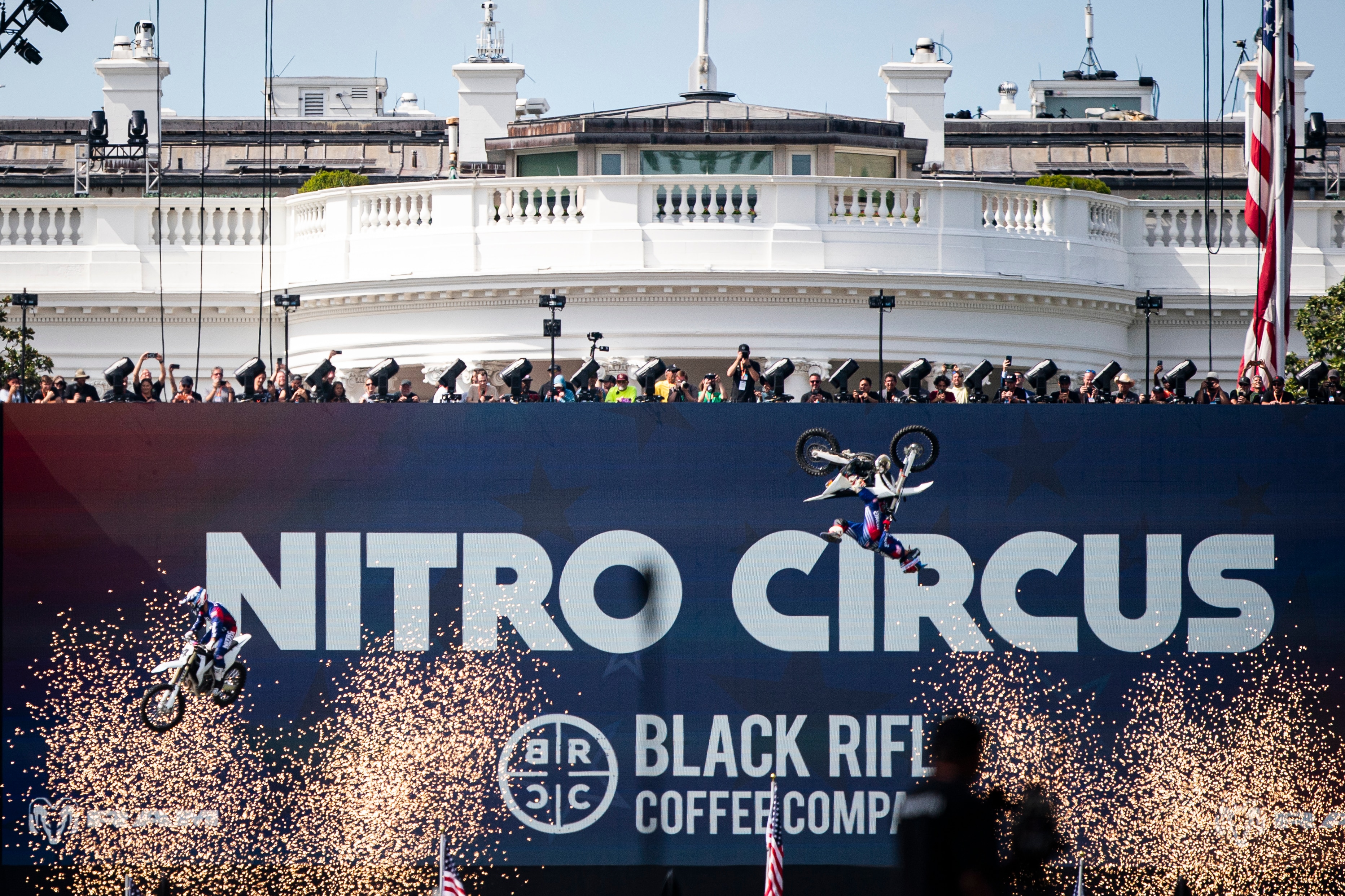 A motorbike flips in the air in front of a giant banner, which covers up the White House in the background.