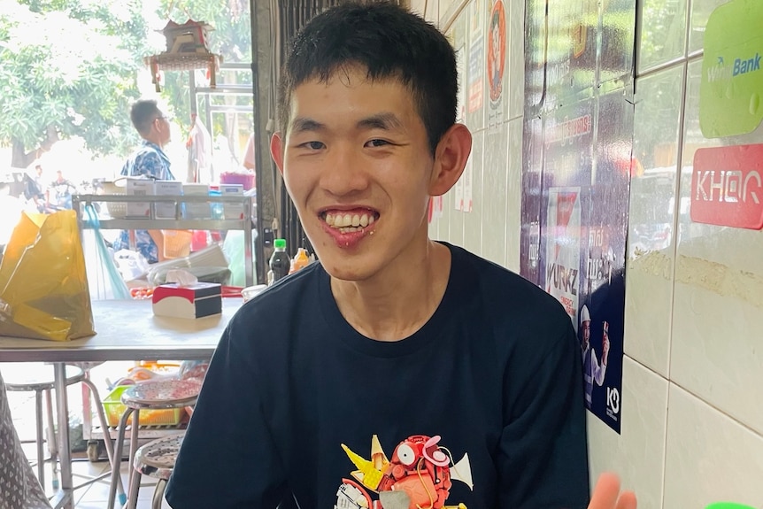 Jefferson Do wears a navy shirt and smiles in front of a plate of food at a restaurant.