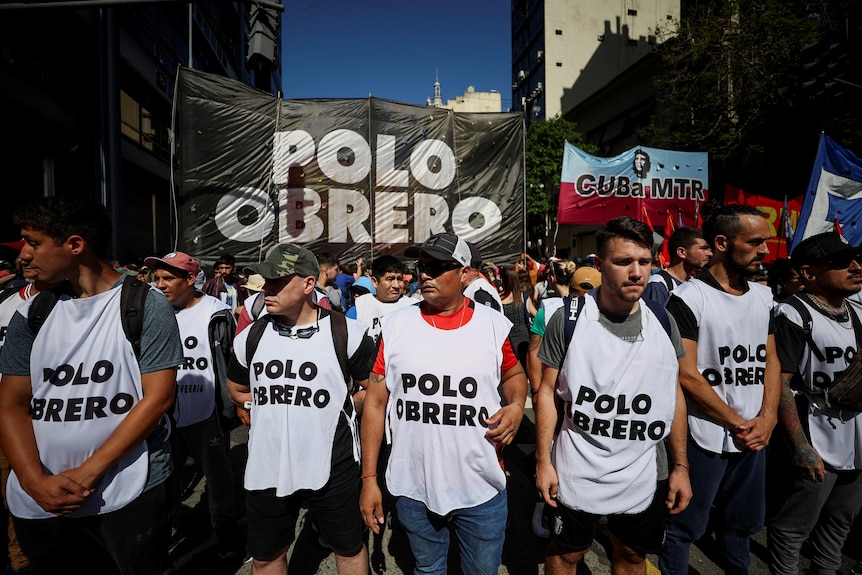 A group of people walk in a line wearing white shirts that say "Polo Obrero" in black.