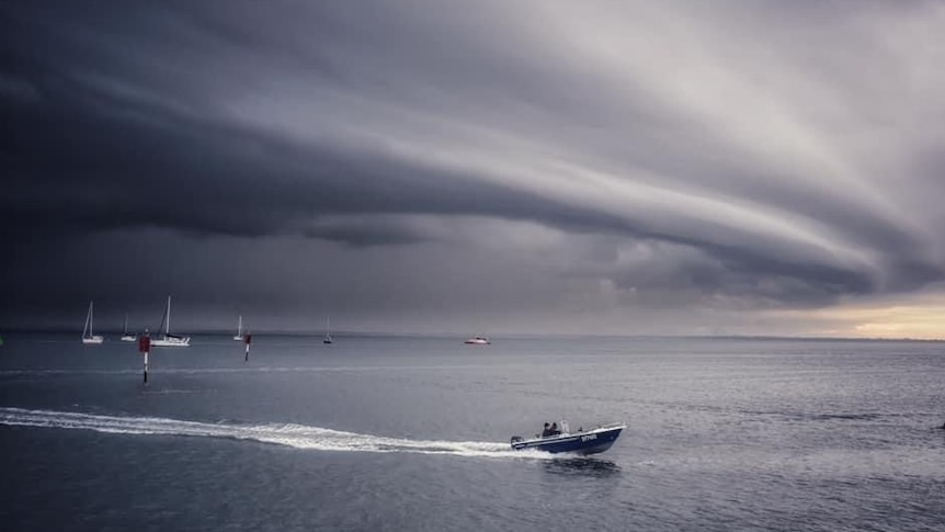 A tinnie drives away from ominous storm clouds.