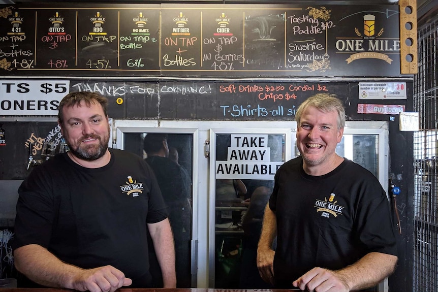 Head Brewers of One Mile Brewery wearing black t-shirts and standing behind a bar
