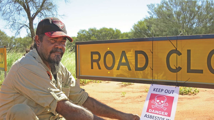 Warlpiri ranger Preston Kelly erects an asbestos warning sign near a walking track in Yuendumu