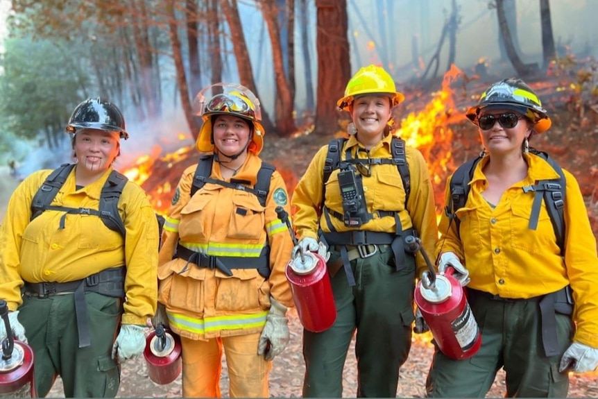 Four women smiling with fire burning behind them