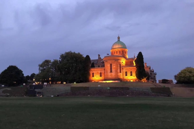A sandstone building lit up at night, with an oval in front of it