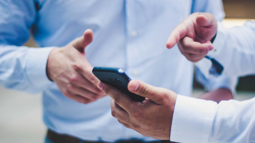 Set of hands belong to two people gesturing towards a smart phone